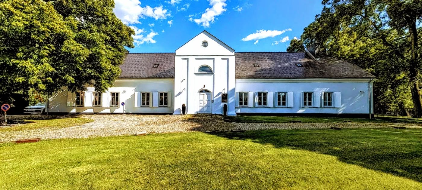 Elewacja frontowa zabytkowego Dworku Wierzenica z klasycznym gankiem na tle słonecznego nieba