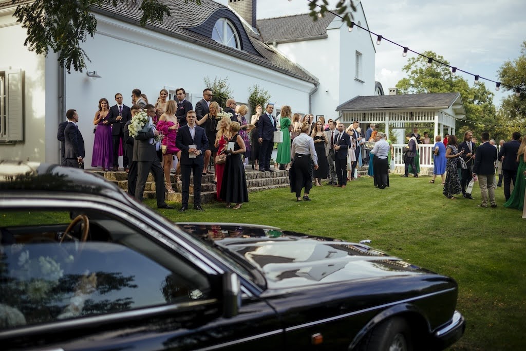 Eleganccy goście weselni zgromadzeni przed dworkiem obok zabytkowego czarnego auta